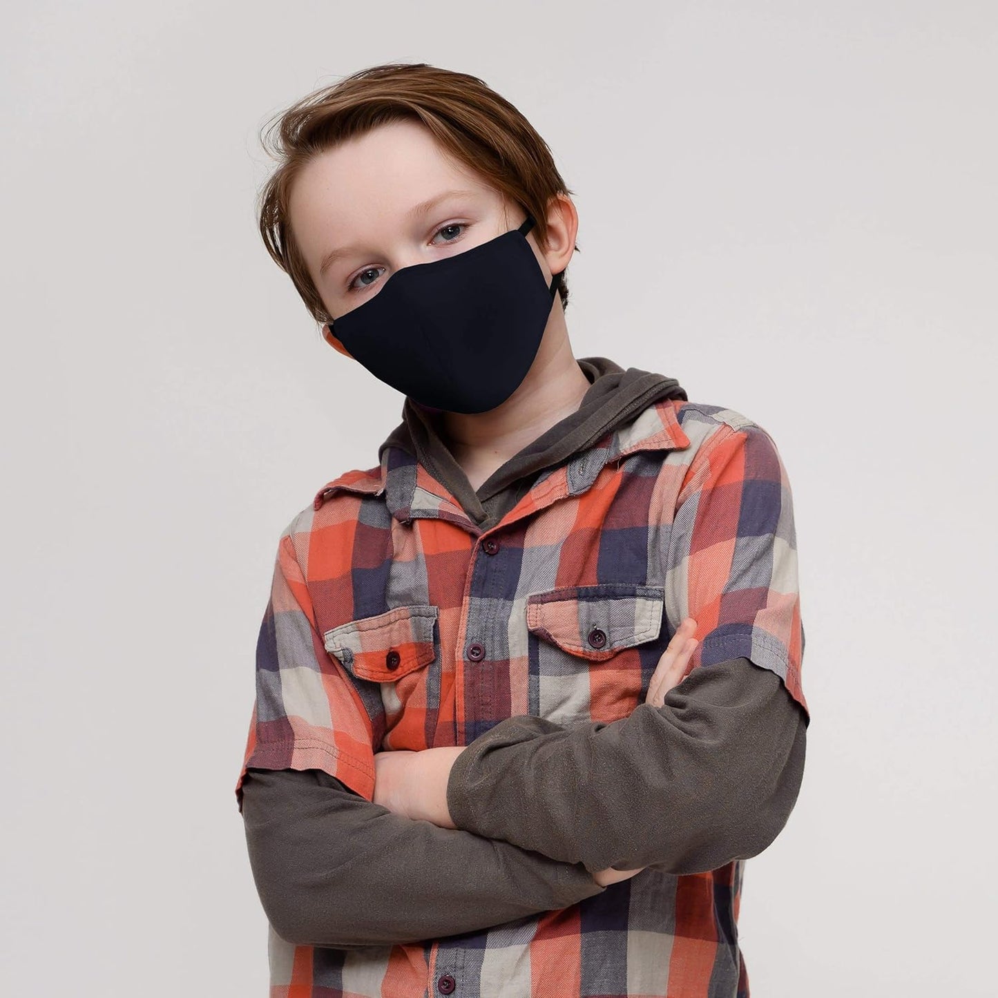Child wearing a black face mask and plaid shirt against a plain background