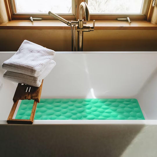 Green bath mat with textured surface in a bathtub next to a stack of towels.