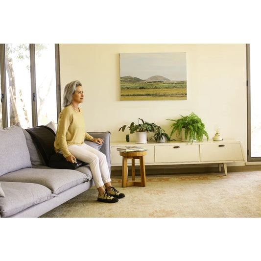 Woman sitting on a couch in a modern living room with plants and a painting.