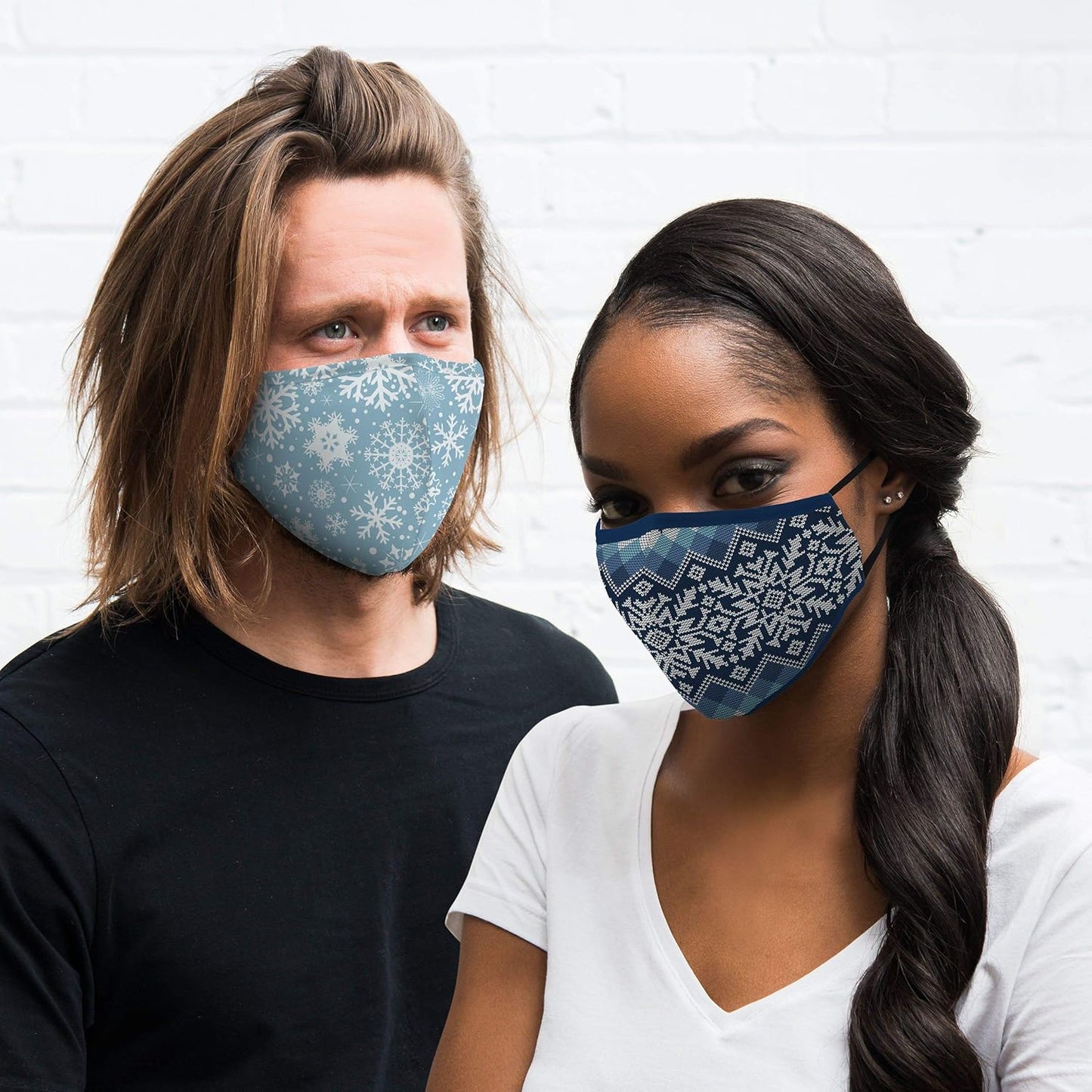 Two people wearing blue patterned face masks against a white brick wall.