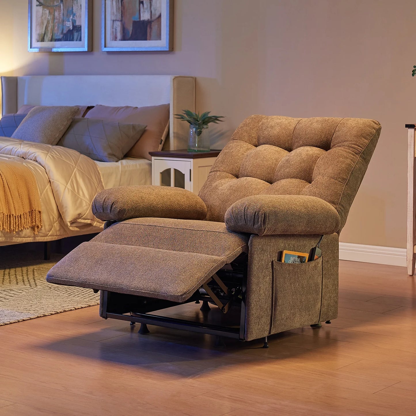 Brown recliner chair in a living room setting with a bed and framed pictures in the background.