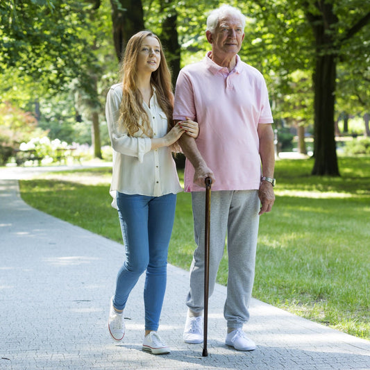 Woman walking with an elderly man using a cane in a park