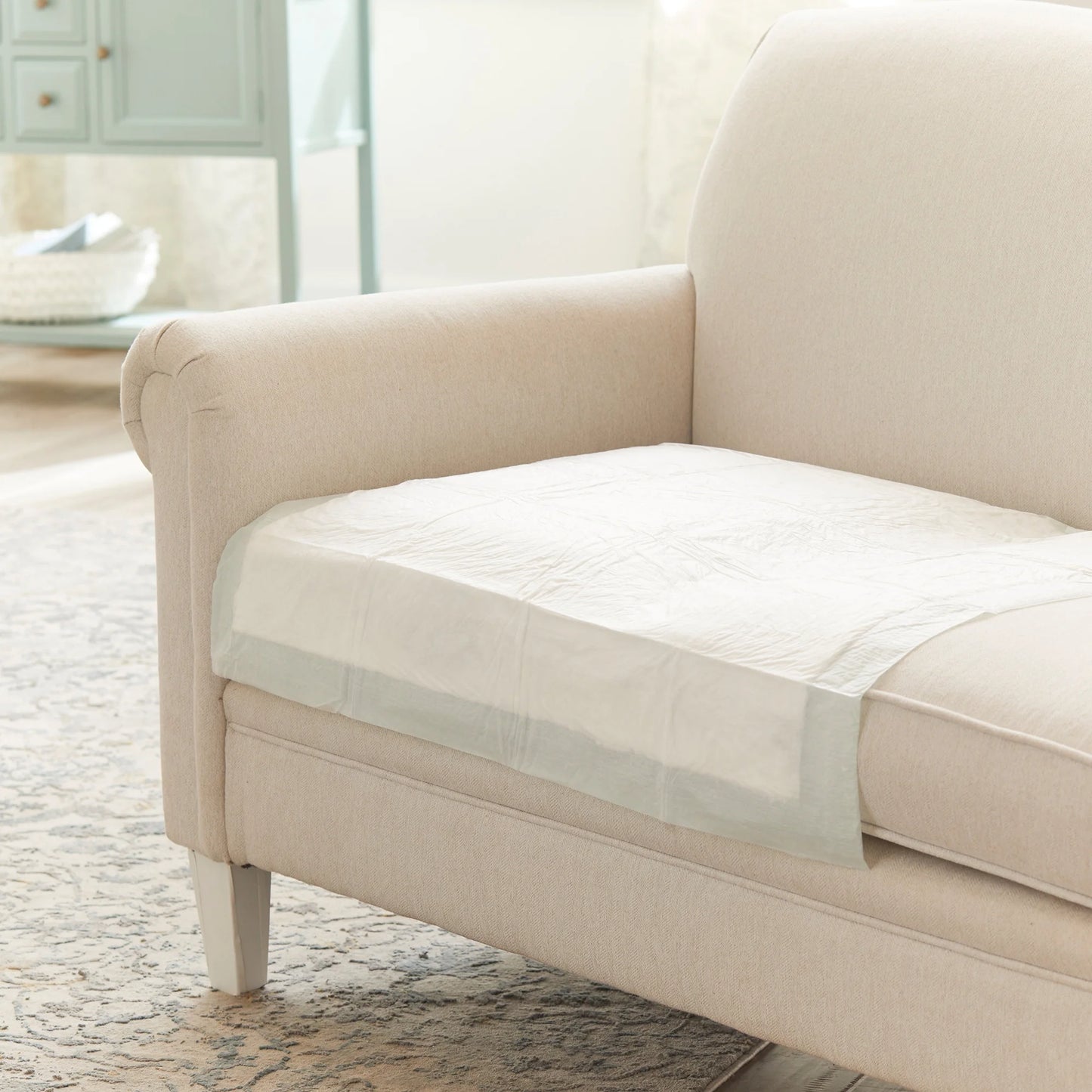Beige sofa with a protective cover on a wooden floor in a living room setting.