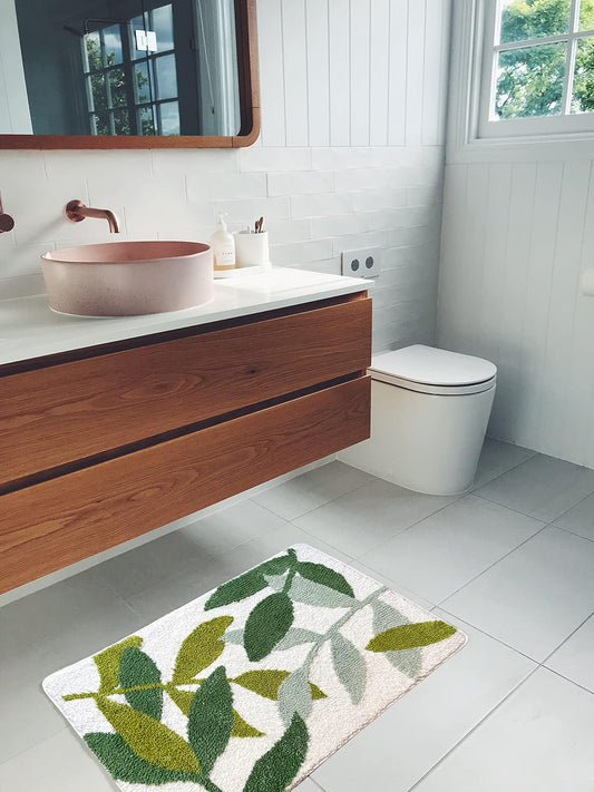 Bathroom with wooden vanity, pink sink, and white toilet with a green leaf-patterned rug on the floor.