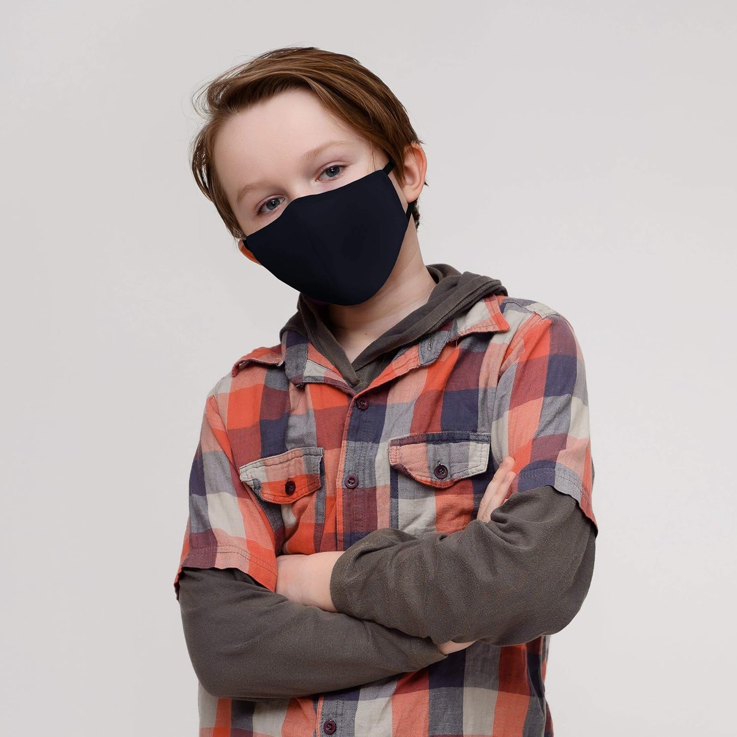 Child wearing a black face mask and plaid shirt against a plain background

