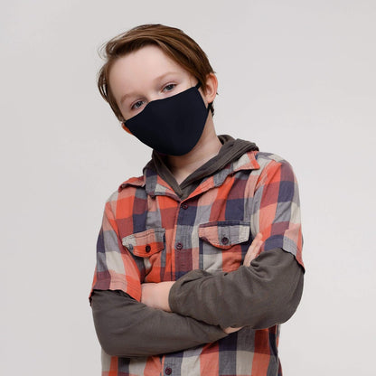 Child wearing a black face mask and plaid shirt against a plain background

