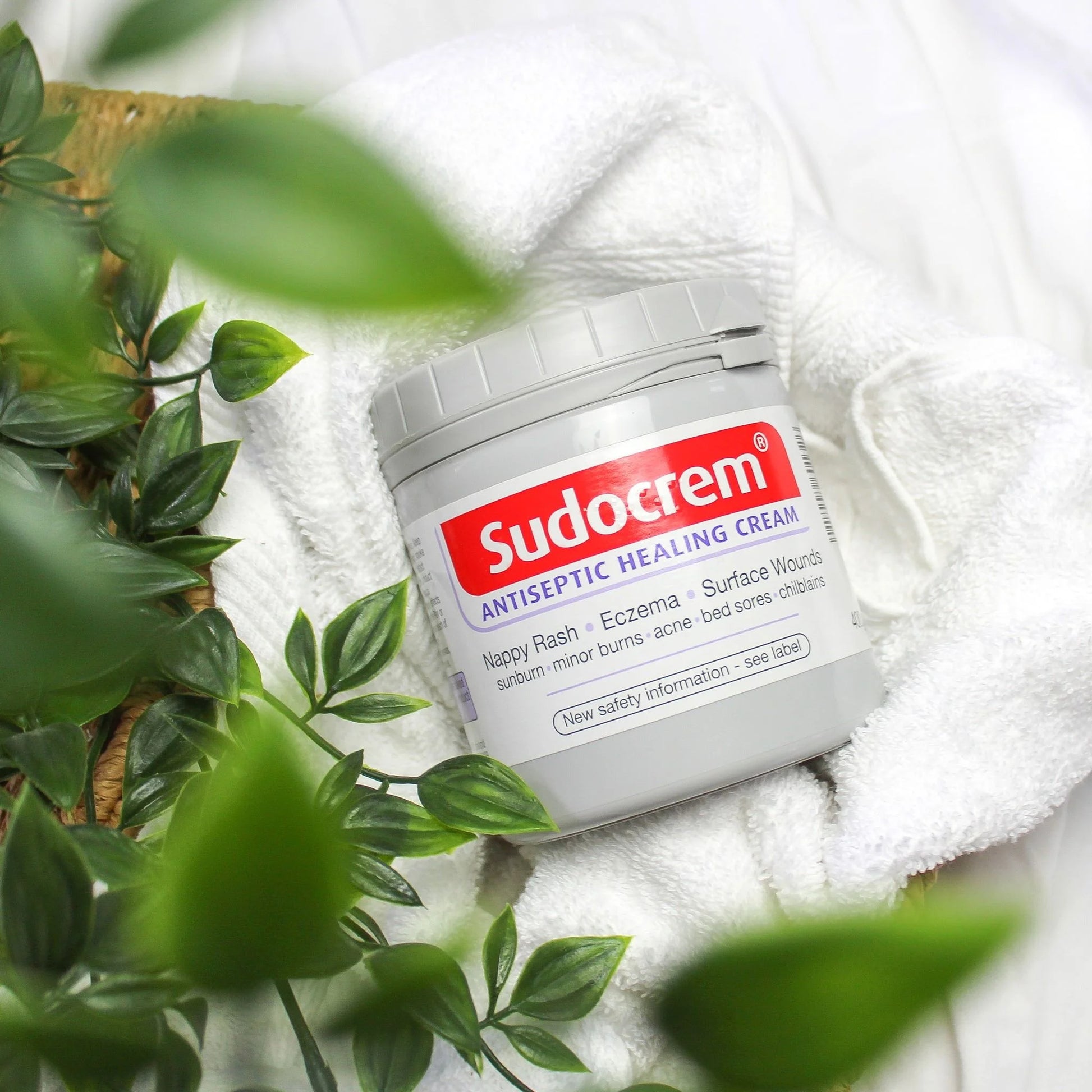 Sudocrem antiseptic healing cream jar on a white towel with green leaves in the foreground


