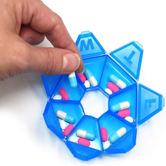 Blue pill organizer with colorful pills being held by a hand on a white background


