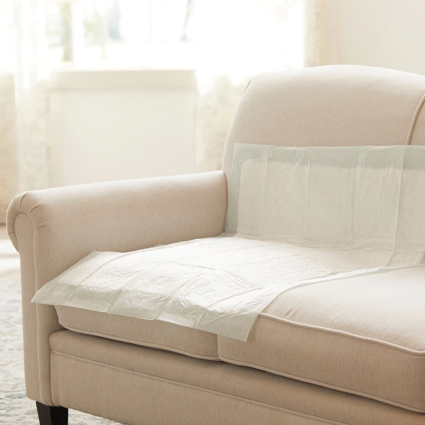 Beige sofa with a white quilt draped over it in a bright room.