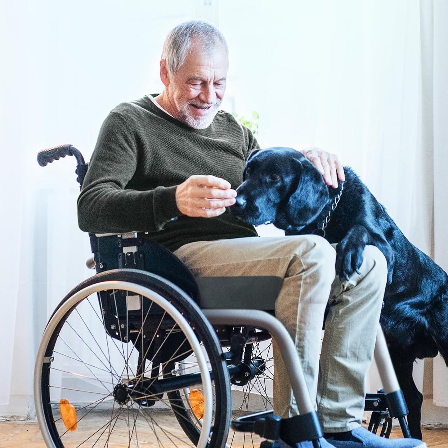 Man in a wheelchair with a black dog indoors

