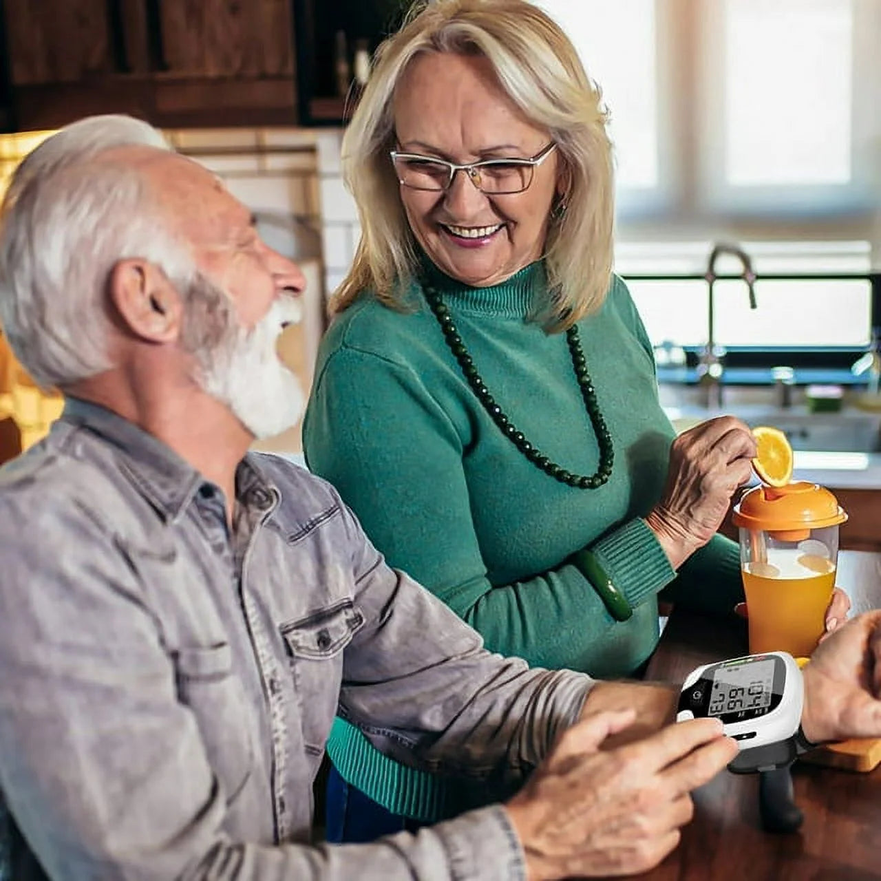 Senior couple in a kitchen with a woman squeezing an orange into a blender.

