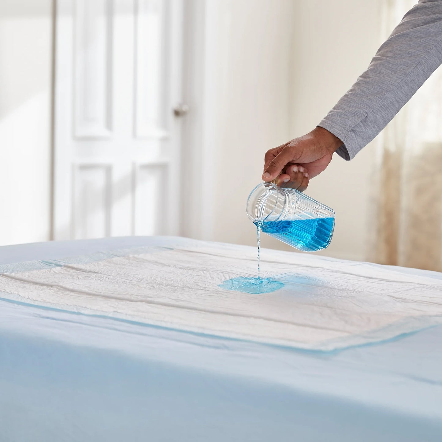 Person pouring blue liquid onto a mattress protector