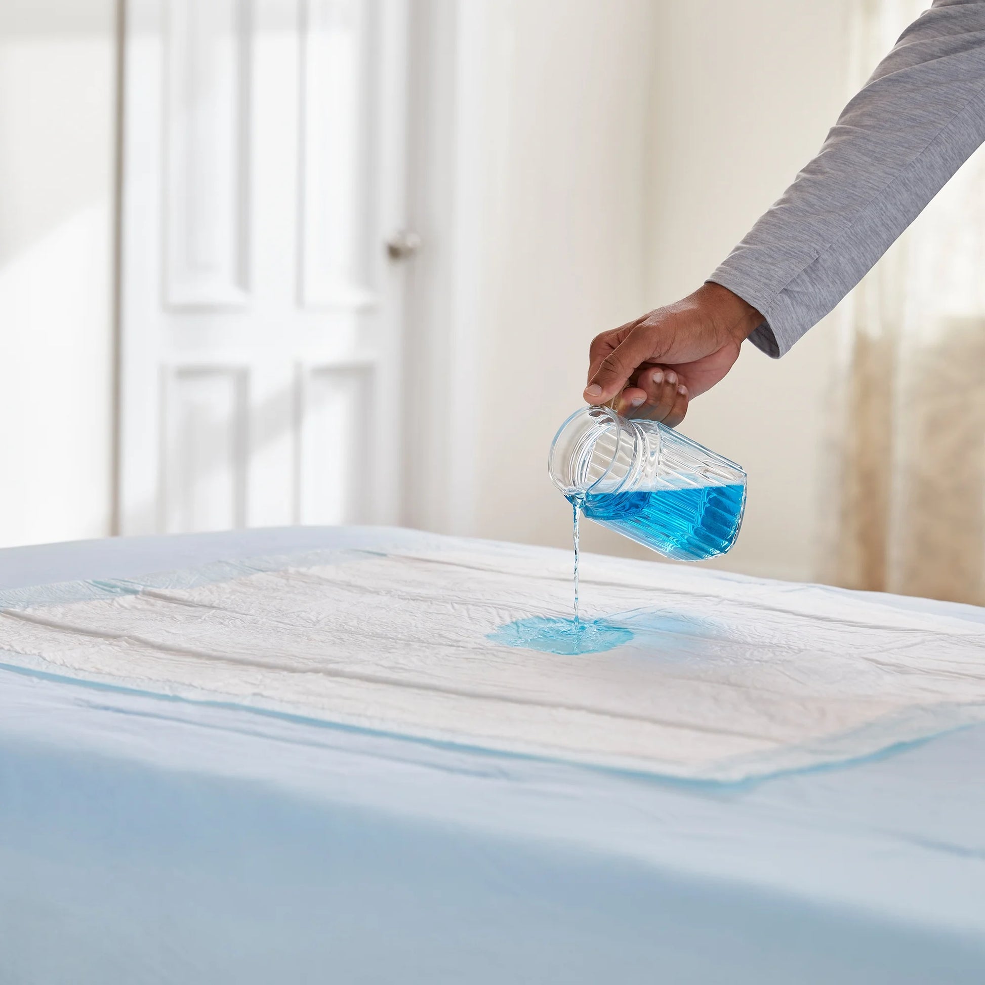 Person pouring blue liquid onto a mattress protector