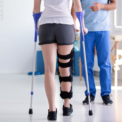 Person using crutches with a knee brace in a clinical setting

