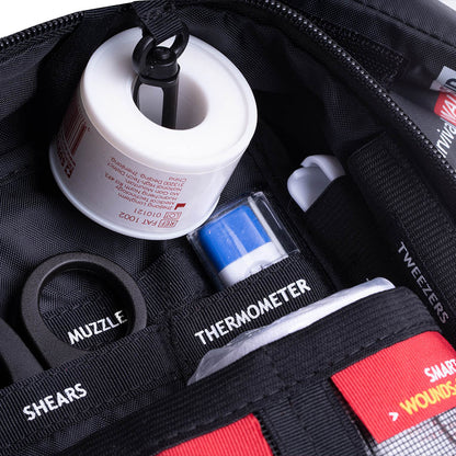 First aid kit contents including a thermometer, bandages, and scissors in a black bag.


