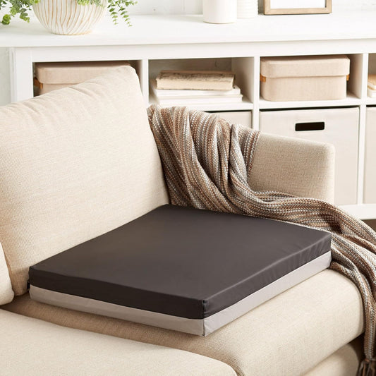 Brown cushion on a beige sofa with a blanket draped over it, in a room with shelves and books.

