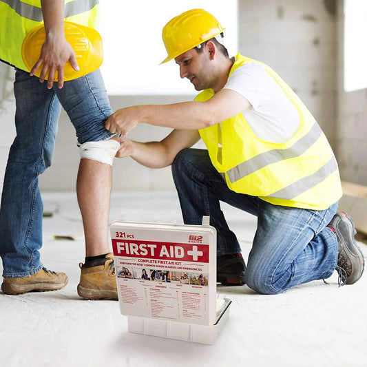Person applying bandage to another person's leg with a first aid kit on a construction site.

