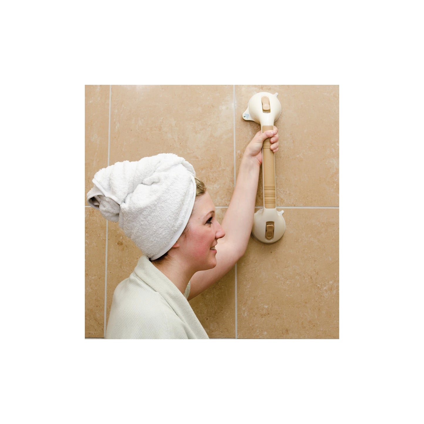 A woman with a white towel wrapped around her head reaches up to use a wall-mounted grab bar on beige tiled bathroom walls.
