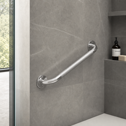 A curved chrome safety grab bar mounted on a gray tiled bathroom wall next to a glass door and built-in shelf with toiletries.