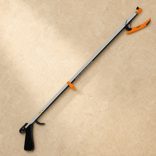 A long-handled grabber tool with a black textured handle, silver metal shaft, and bright orange tips, photographed diagonally on a beige stone-textured background.
