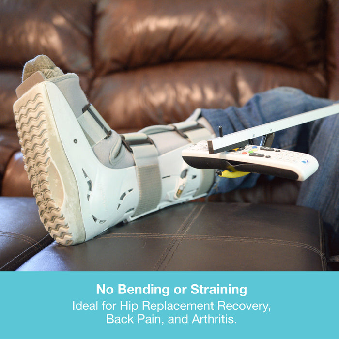 A white and gray leg cast with a white remote control attached, resting on a brown leather couch. A person's leg in blue jeans is visible, and a text banner at the bottom reads 'No Bending or Straining Ideal for Hip Replacement Recovery, Back Pain, and Arthritis.