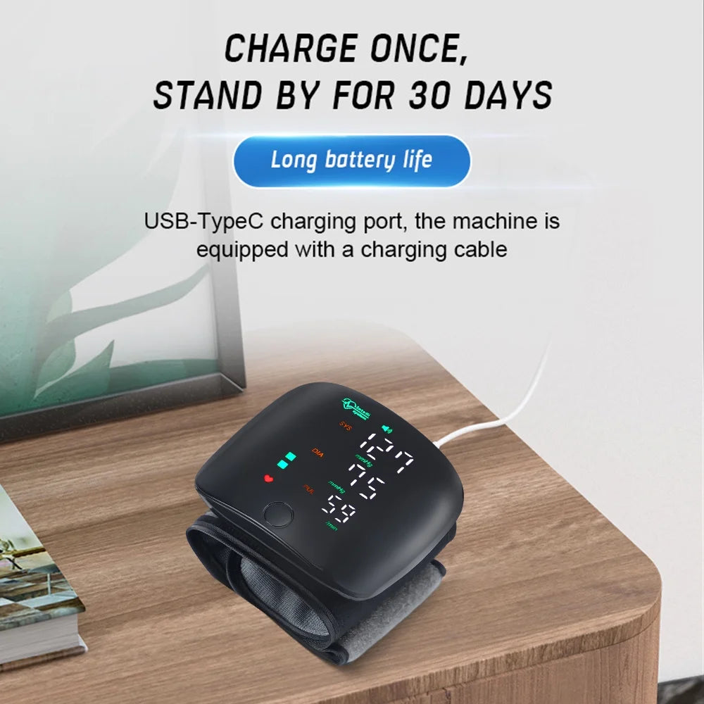 Digital blood pressure monitor on a wooden surface with text about battery life and charging port.

