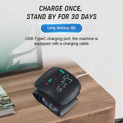 Digital blood pressure monitor on a wooden surface with text about battery life and charging port.

