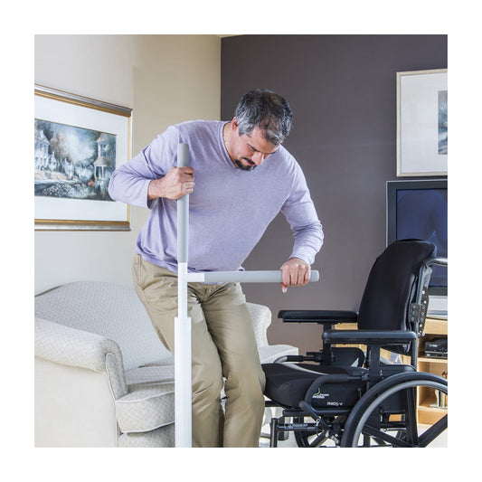 Man using a white floor rail in a living room with a wheelchair and television in the background.