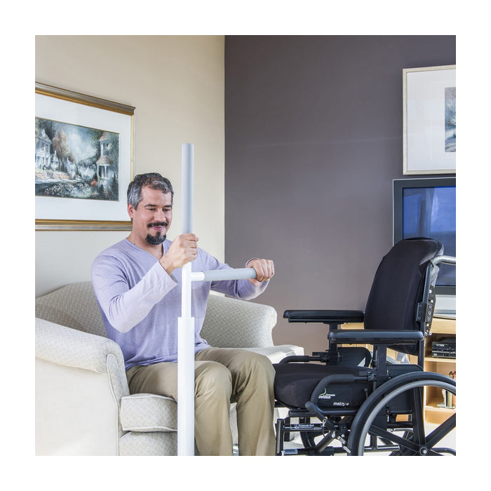 Man using a white floor rail in a living room with a wheelchair and television in the background.