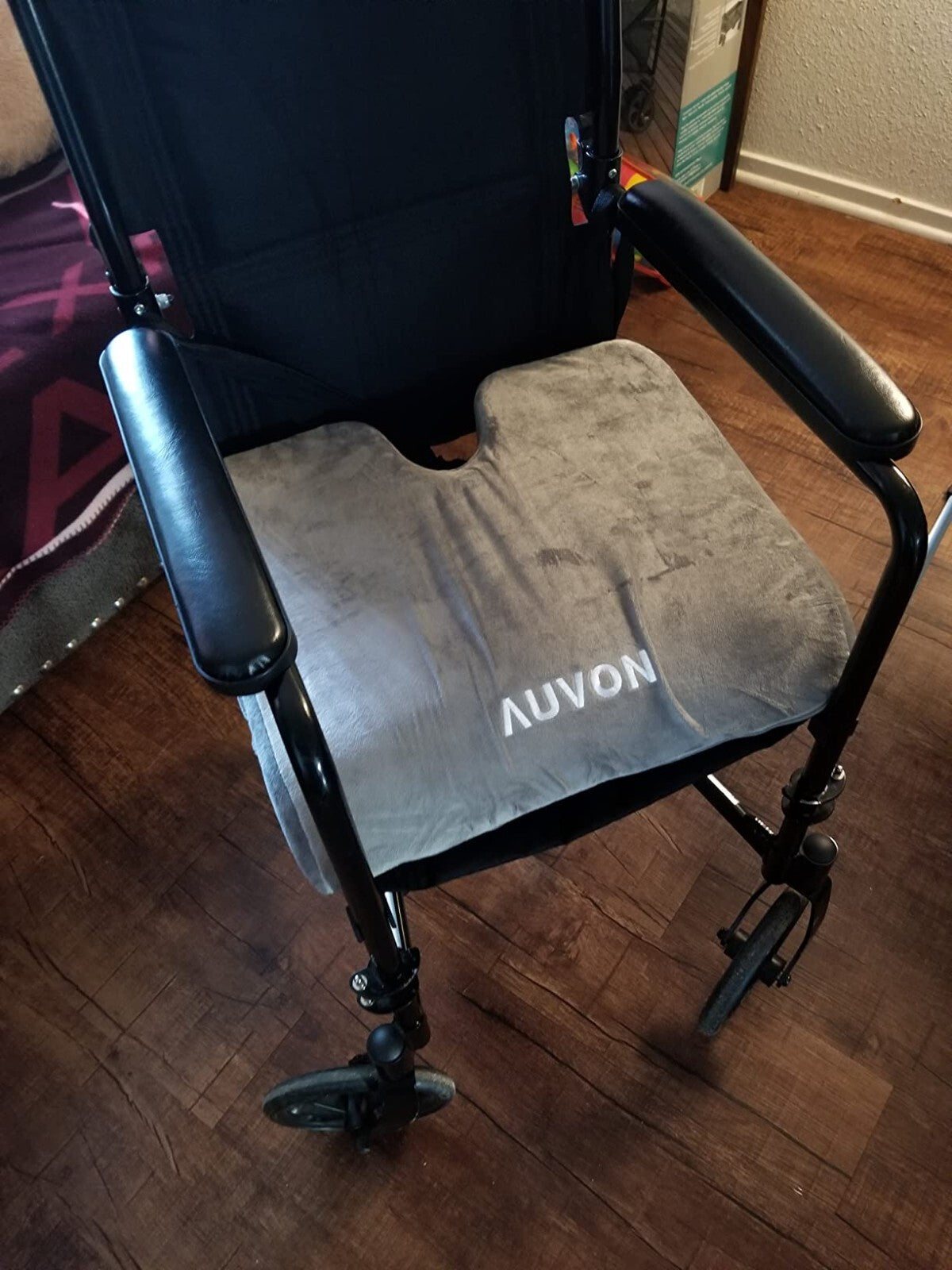 Black wheelchair with gray cushion on a wooden floor

