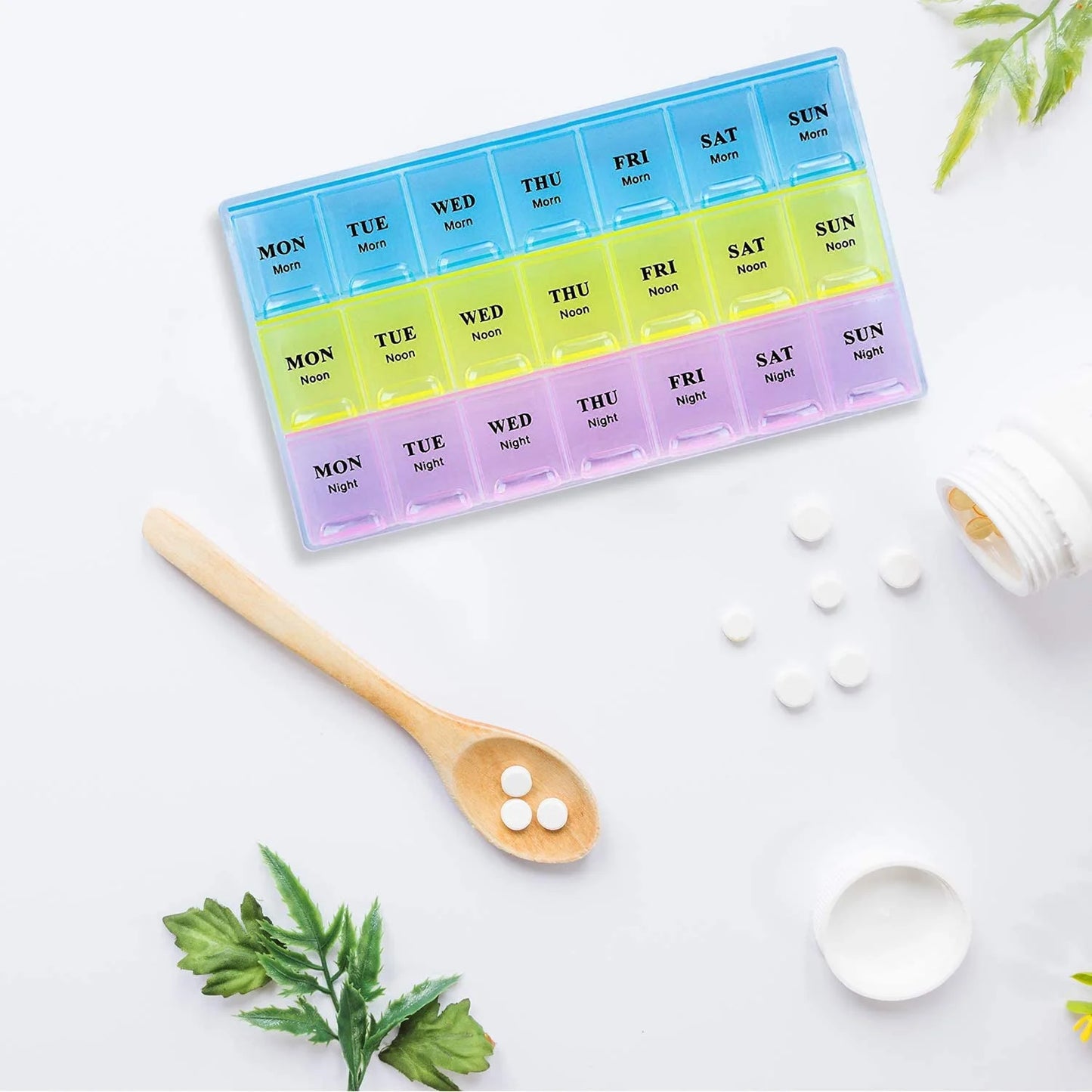 Weekly pill organizer with colorful compartments on a white surface with tablets and a spoon.


