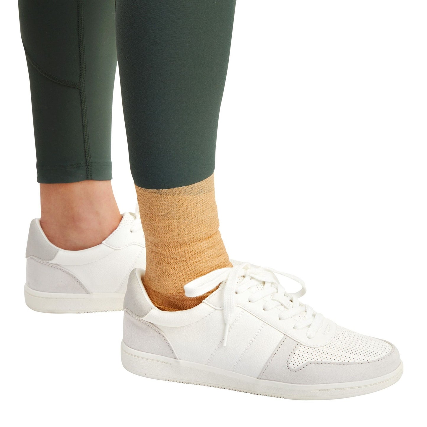 White sneakers worn with green leggings showing ankle wrapped in bandage on a white background

