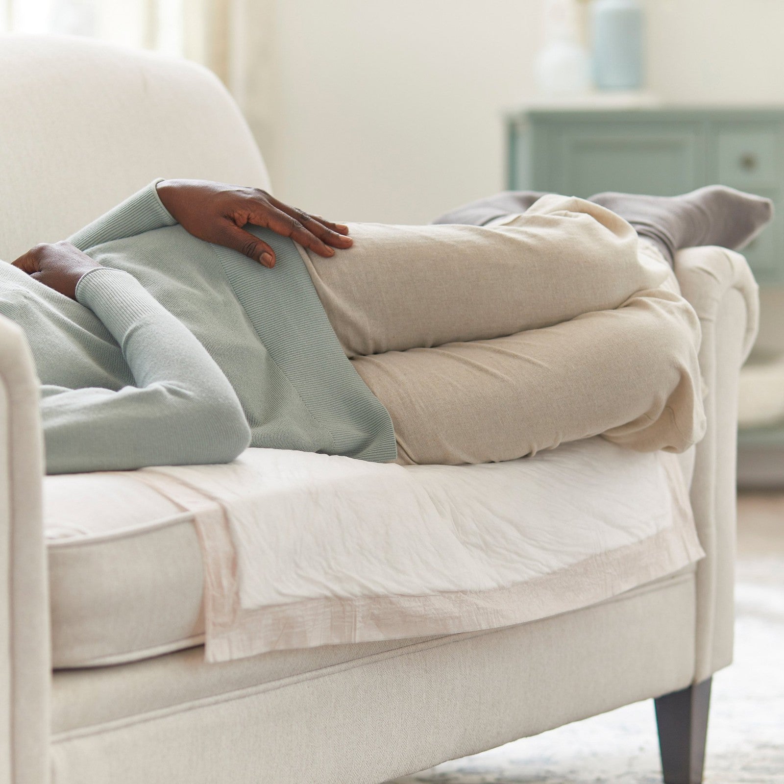 Two people lying on a beige couch with a blanket, in a softly lit room.