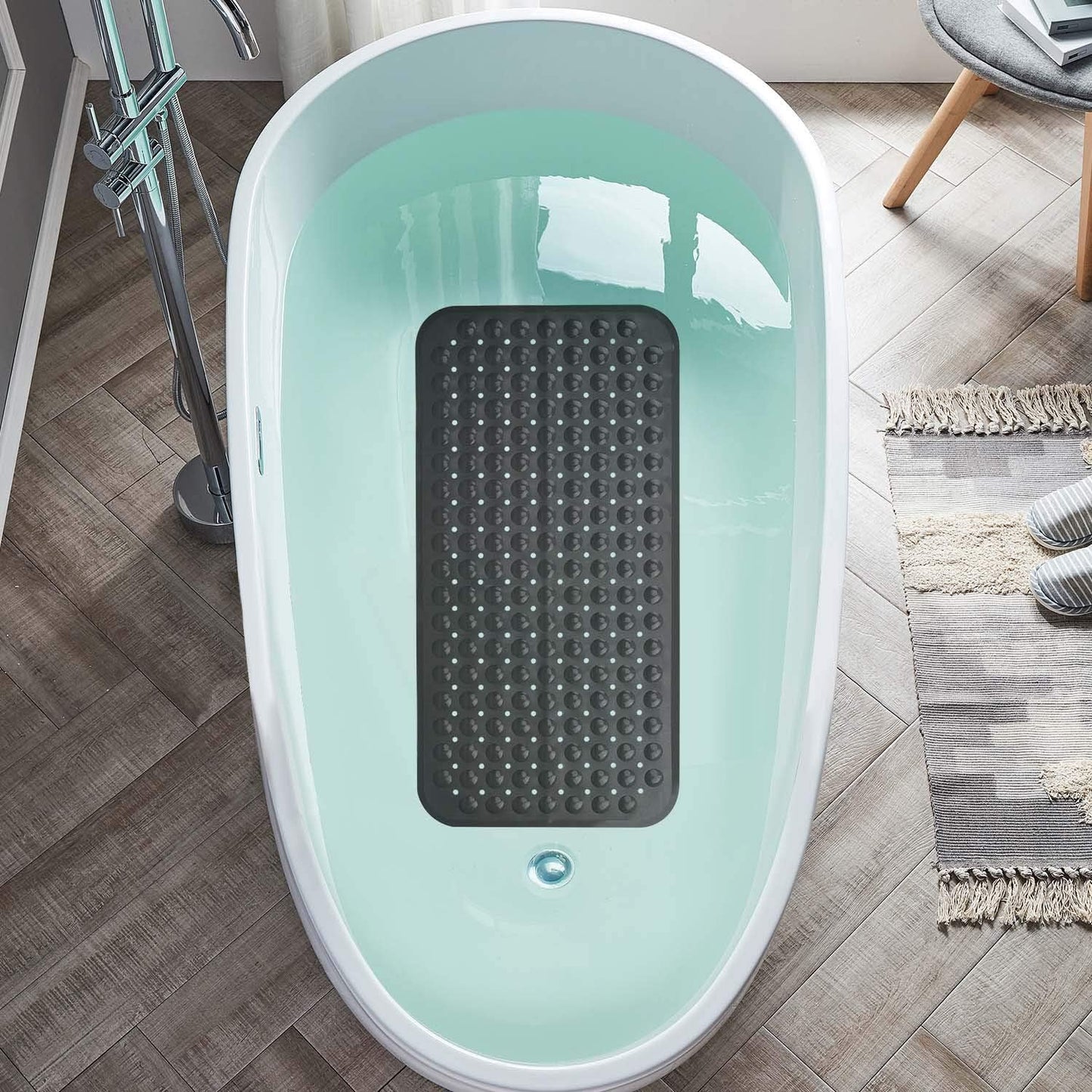 Light blue bathtub with a black textured mat inside on a wooden floor.

