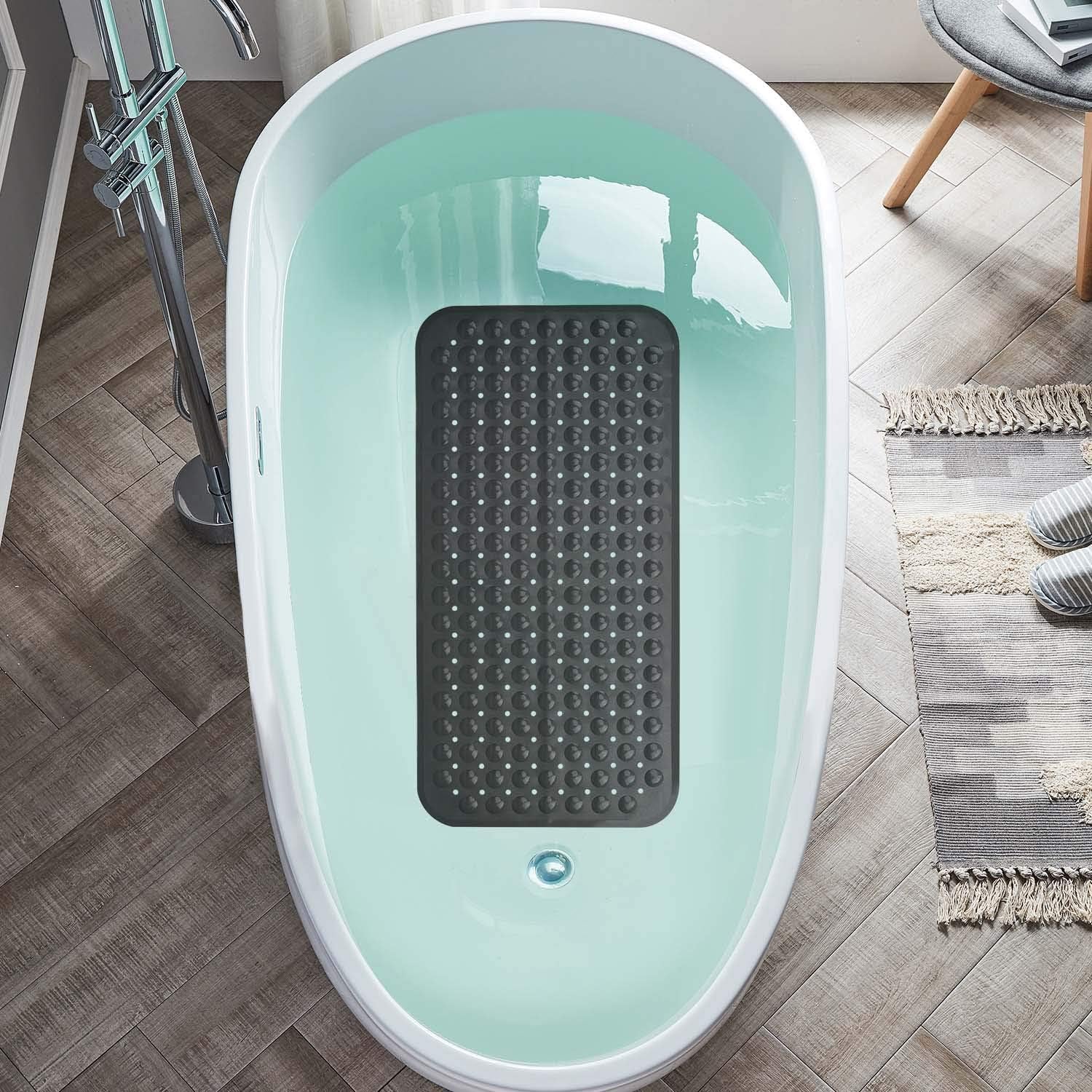 Light blue bathtub with a black textured mat inside on a wooden floor.

