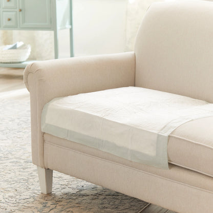 Beige sofa with a protective cover on a wooden floor in a living room setting.