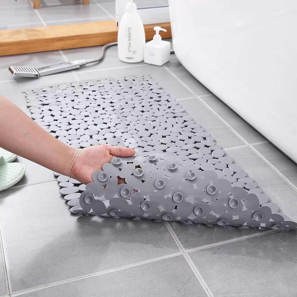 Gray interlocking bath mat on a tiled bathroom floor with a hand holding one piece.